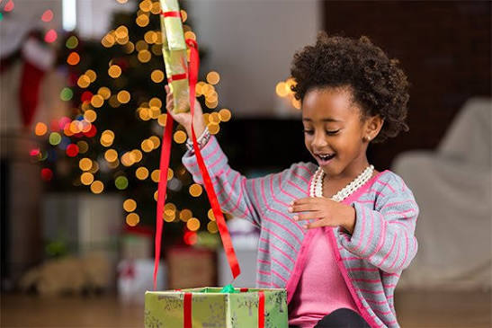 Bambina che apre un regalo accanto a un albero di Natale